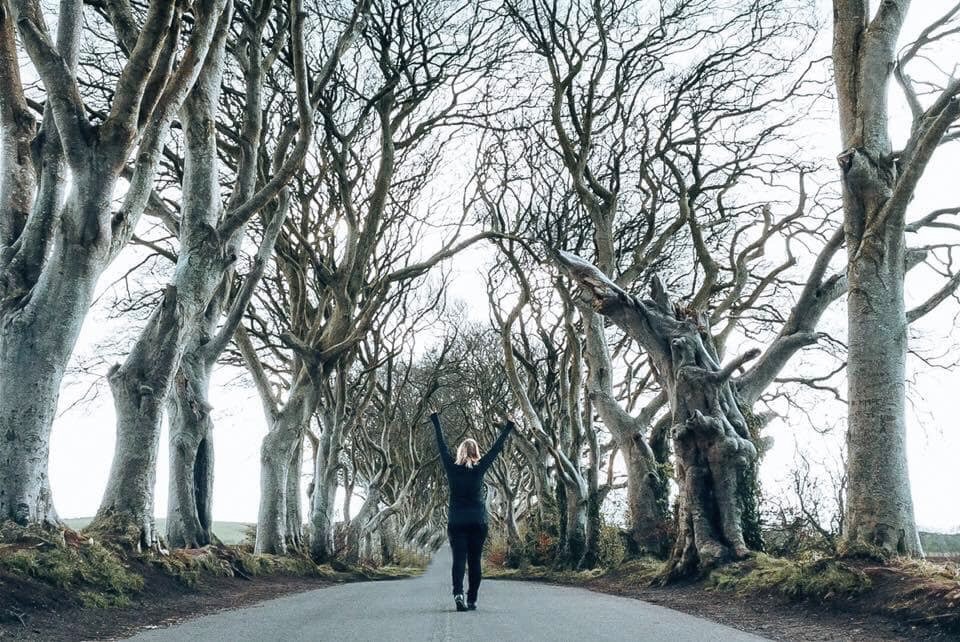 Woman standing in middle of Dark Hedges raising hands in peace signs