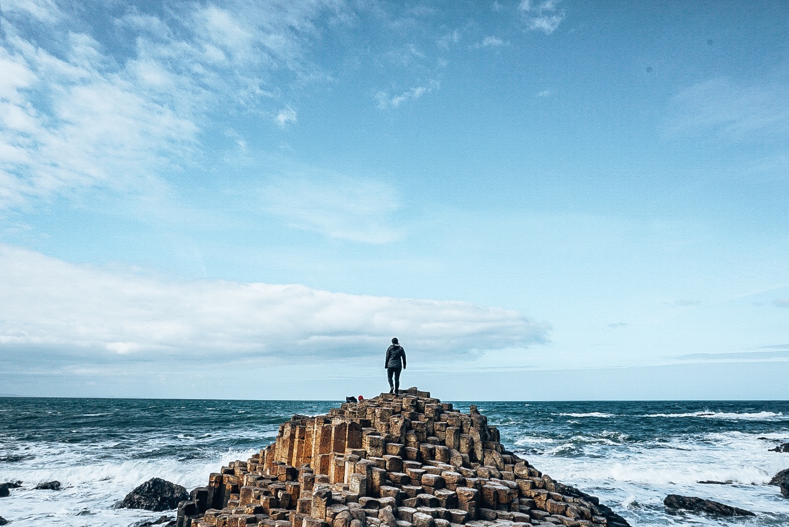 Woman standing on small mountain of hexagonal rocks jutting out from the ocean