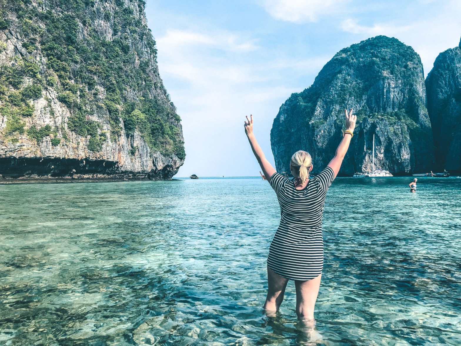 Woman standing in Maya Bay, looking out to the entrance, holding peace signs in the air