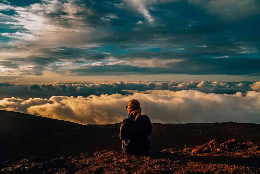 Woman sitting on the edge at sunset over the clouds