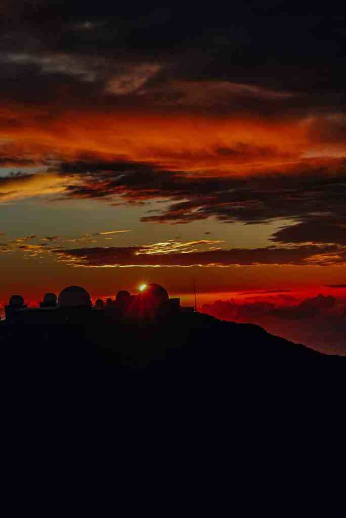 The sun setting behind the observatory, turning the sky bright orange and red