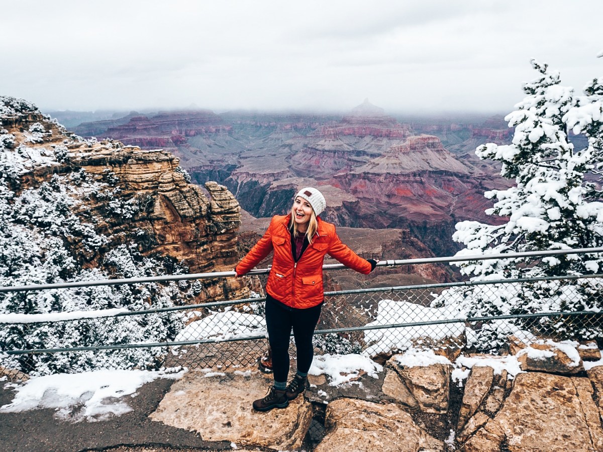 Woman standing along the fenceline at the Grand Canyon during the winter, with the trees and rocked covered in snow
