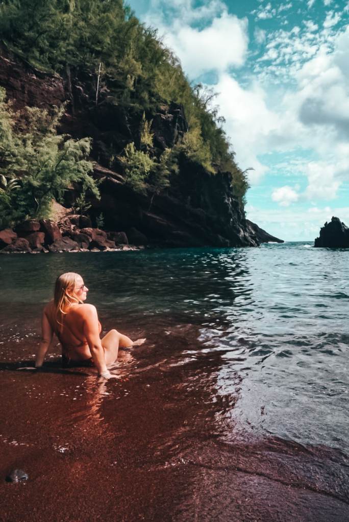 Woman sitting on the red sand beach of Kaihalulu Beach in Maui, looking out to the ocean