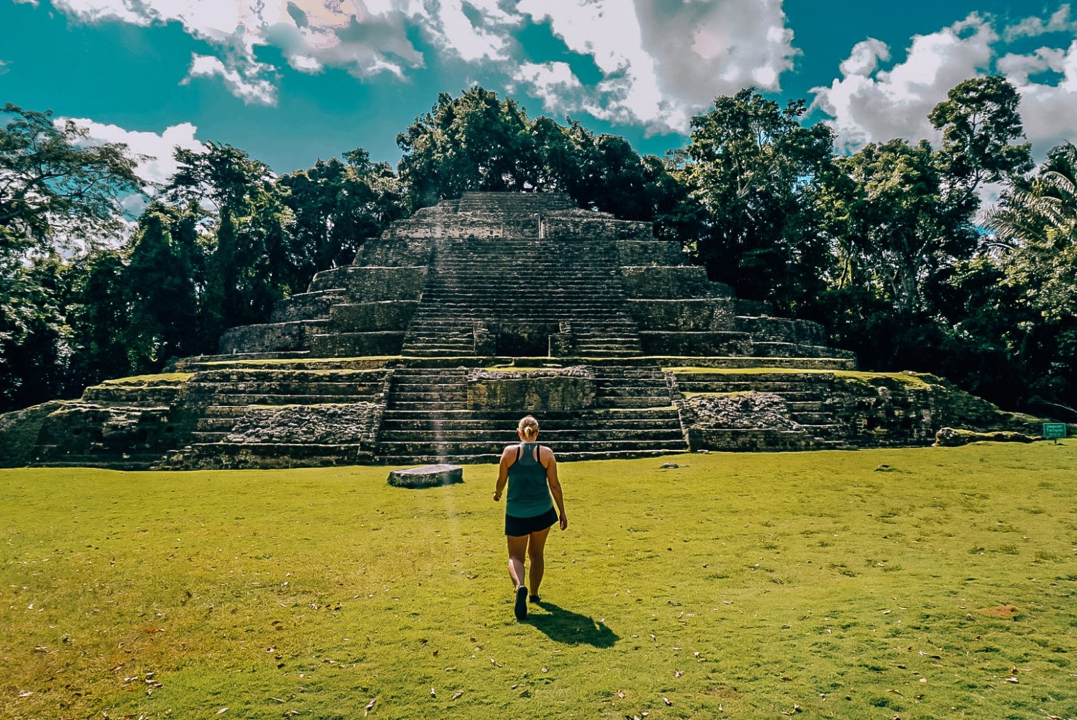 Woman standing in front of a pyramid at the Lamanai ruins in Belize, walking away from camera