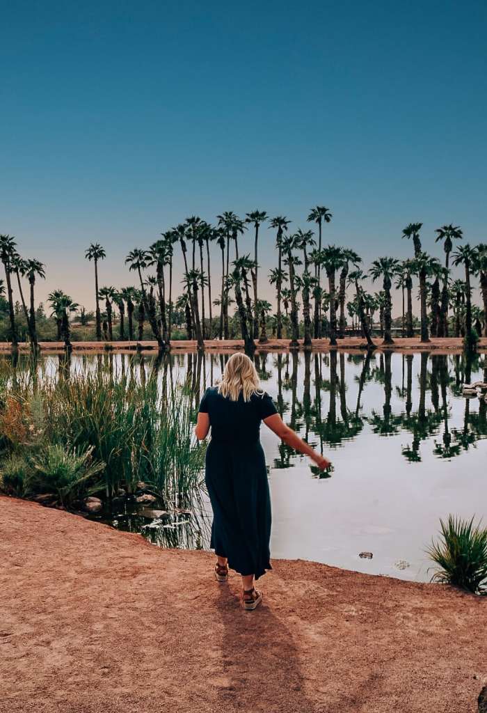 Woman standing in front of water and palm trees at Papago Park in Scottsdale