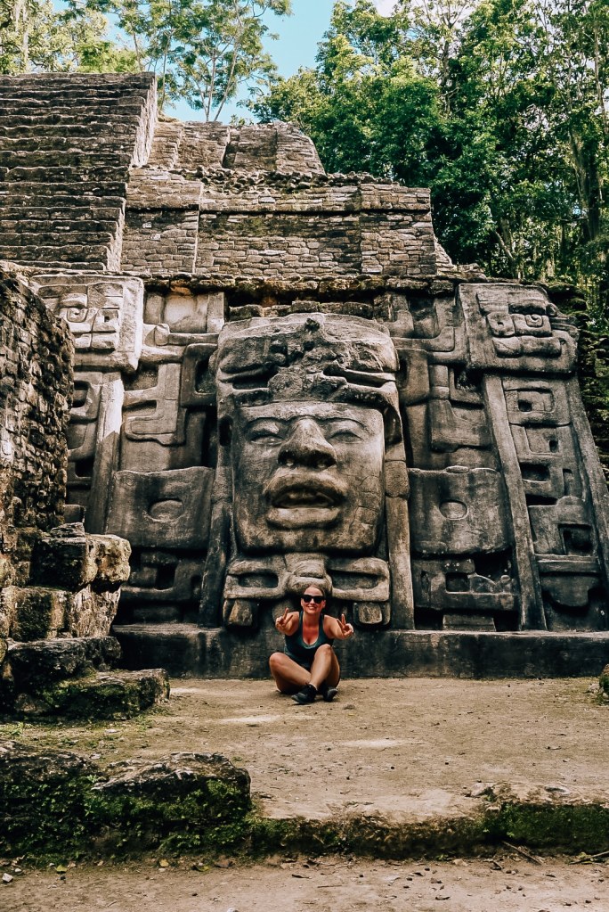 Woman sitting in front of ruin at Lamanai in Belize with giant face carved into it