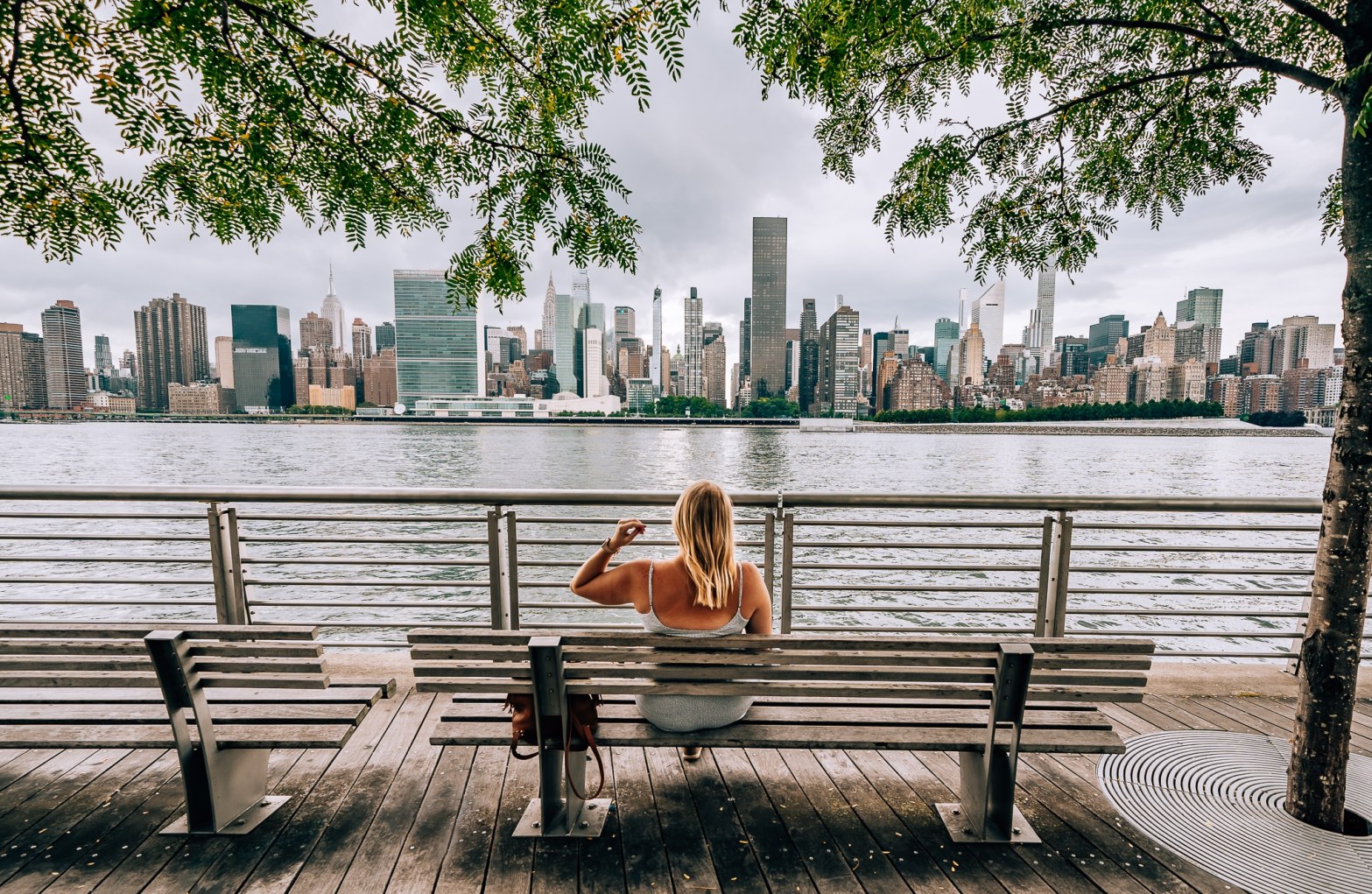 Woman sitting on a bench in Long Island City, Queens, looking out at the waterfront and Manhattan skyline