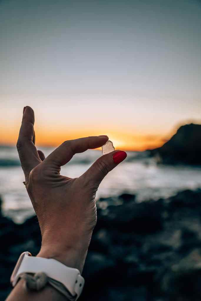 Woman holding up a piece of sea glass found on the beach over the sunset