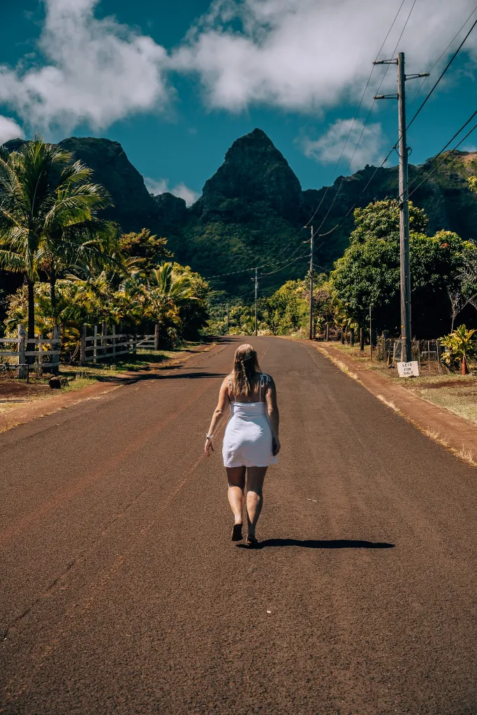 Woman in a white dress standing in the middle of the street looking up to a mountain in Kapa'a town of Kauai
