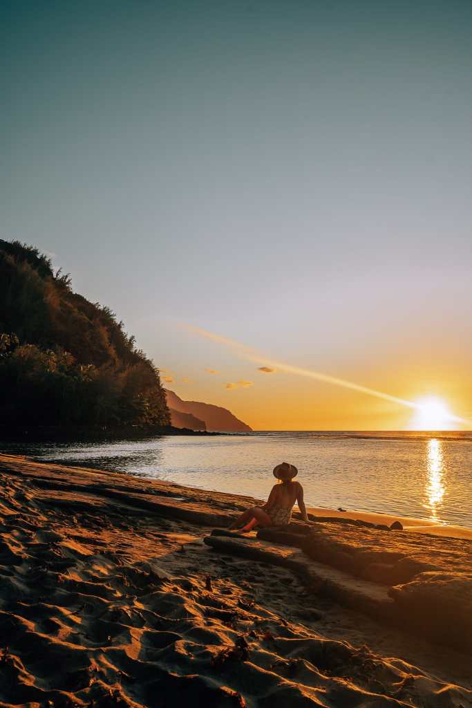 Woman sitting on the beach during sunset at Ke'e Beach in Kauai