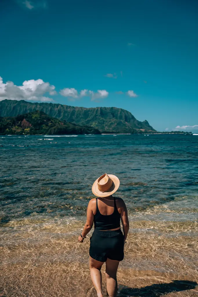 Woman in a hat, black shirt, and black shorts looking out to the beach in the north shore of Kauai