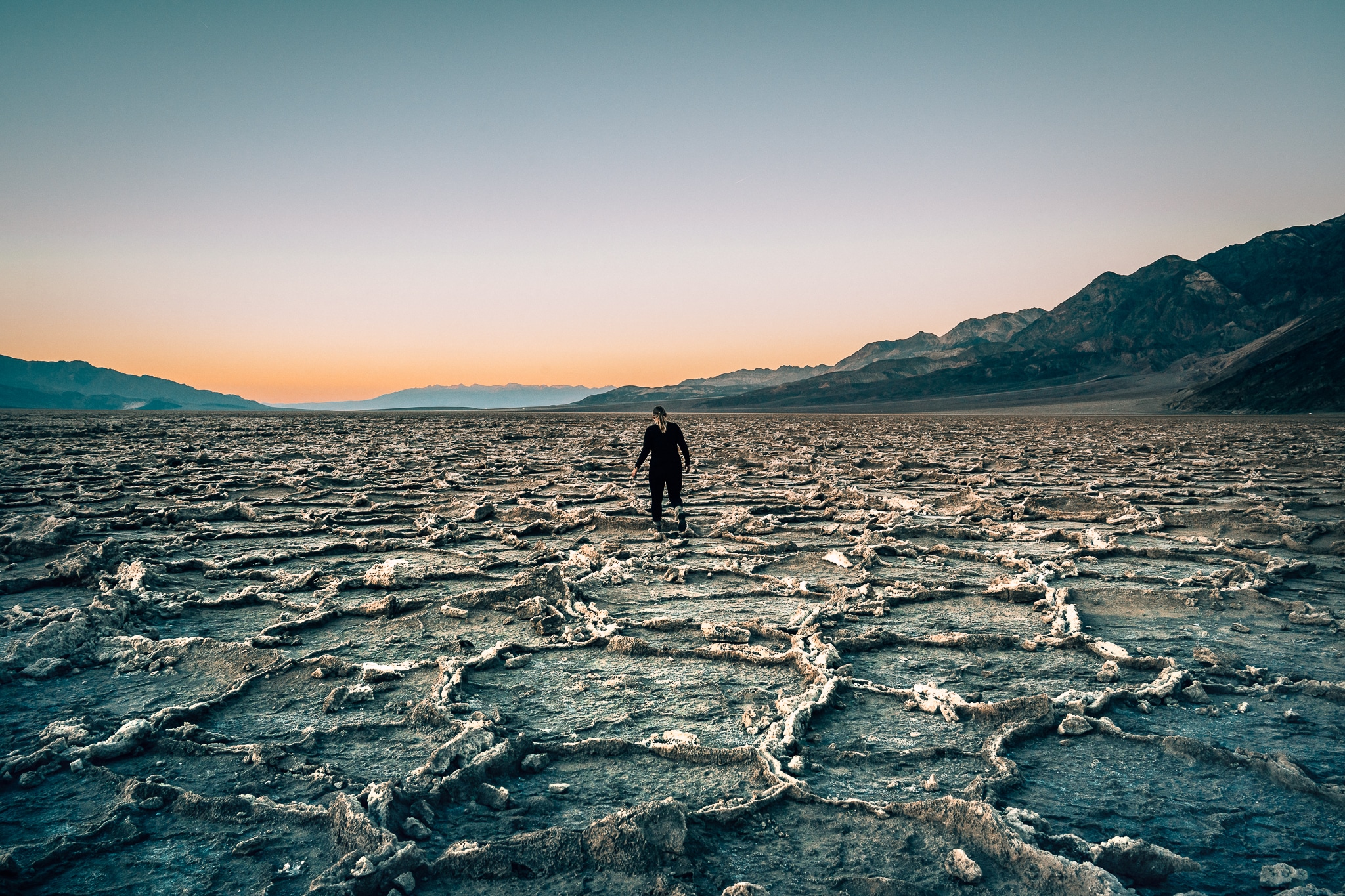 Woman walking along Badwater Basin salt flats at sunset
