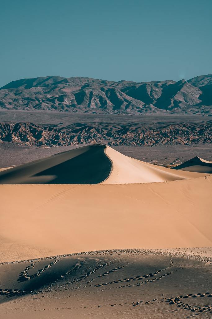 Sand dunes in the sunlight with mountains in the background at Death Valley National Park