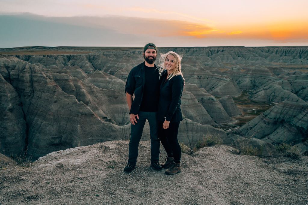 Travel couple standing in front of Badlands at sunrise