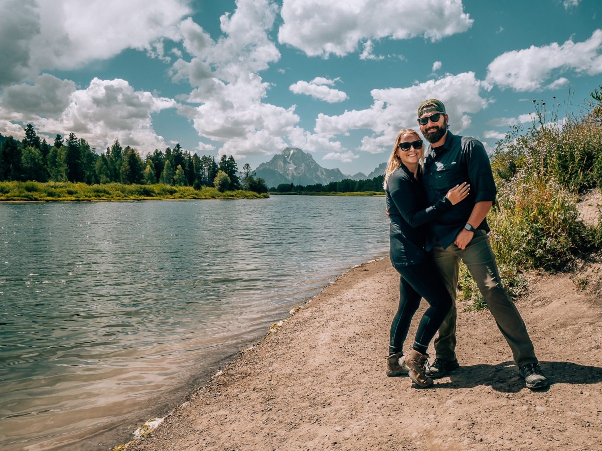 Blonde woman and brunette bearded man standing in front of the Grand Tetons
