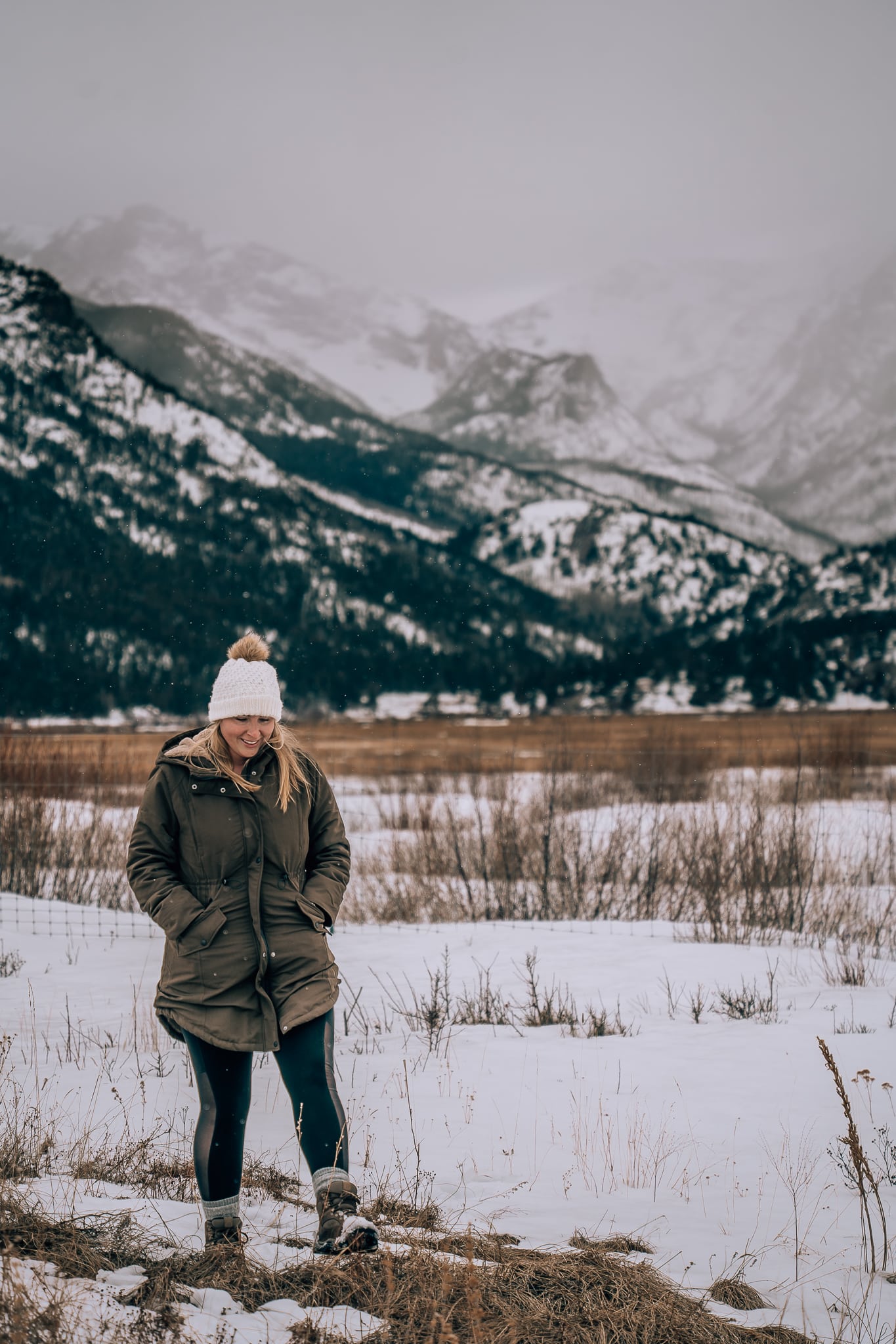 Woman in winter coat and hat walking in front of mountains at Rocky Mountain National Park