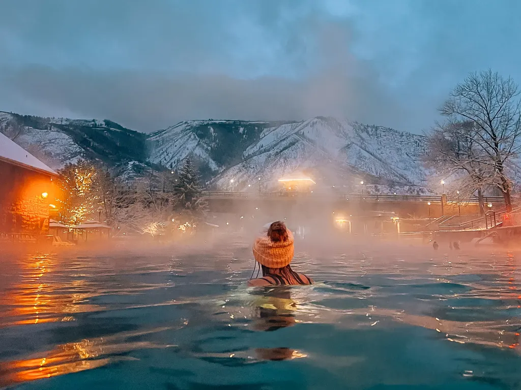 Woman in a hat in the Glenwood Springs Hot Spring pool with the snowy mountains in the background