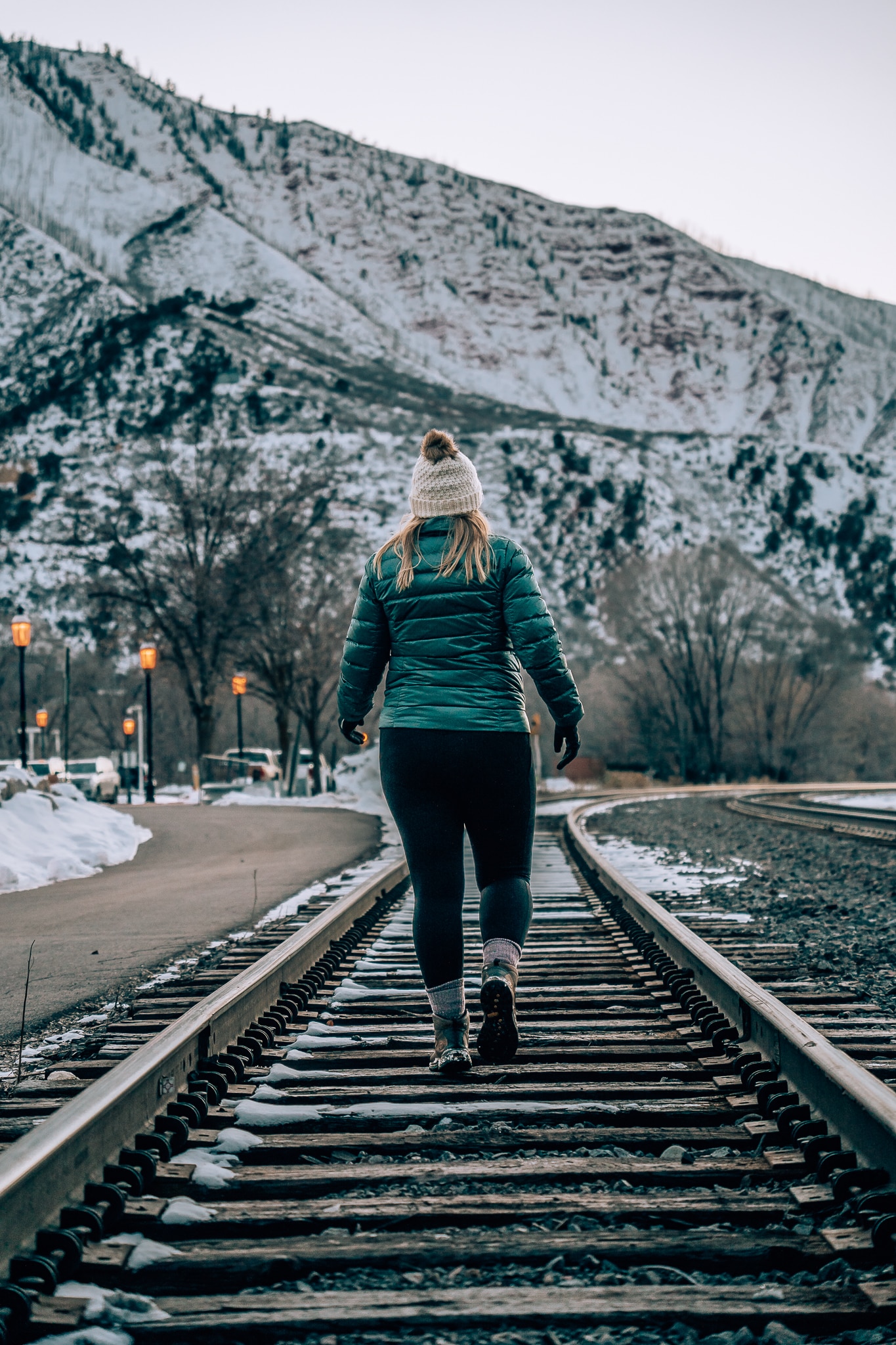Woman in a coat and hat walking along a railroad track with the mountains in the background in Glenwood Springs, Colorado