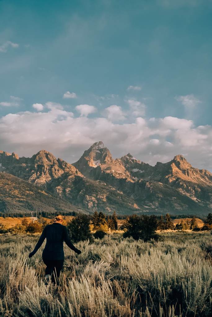 Woman walking in the grass in front of the Teton Mountains