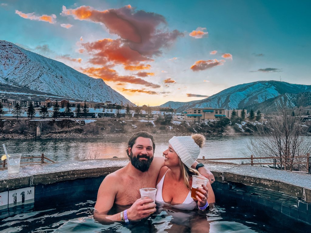 Happy couple drinking beer in one of the pools at Iron Mountain Hot Springs at sunset