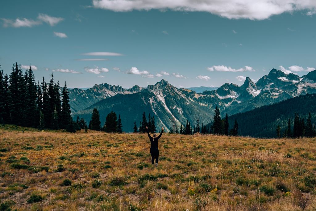 Woman standing in a field raising her hands in front of the Cascade Mountains
