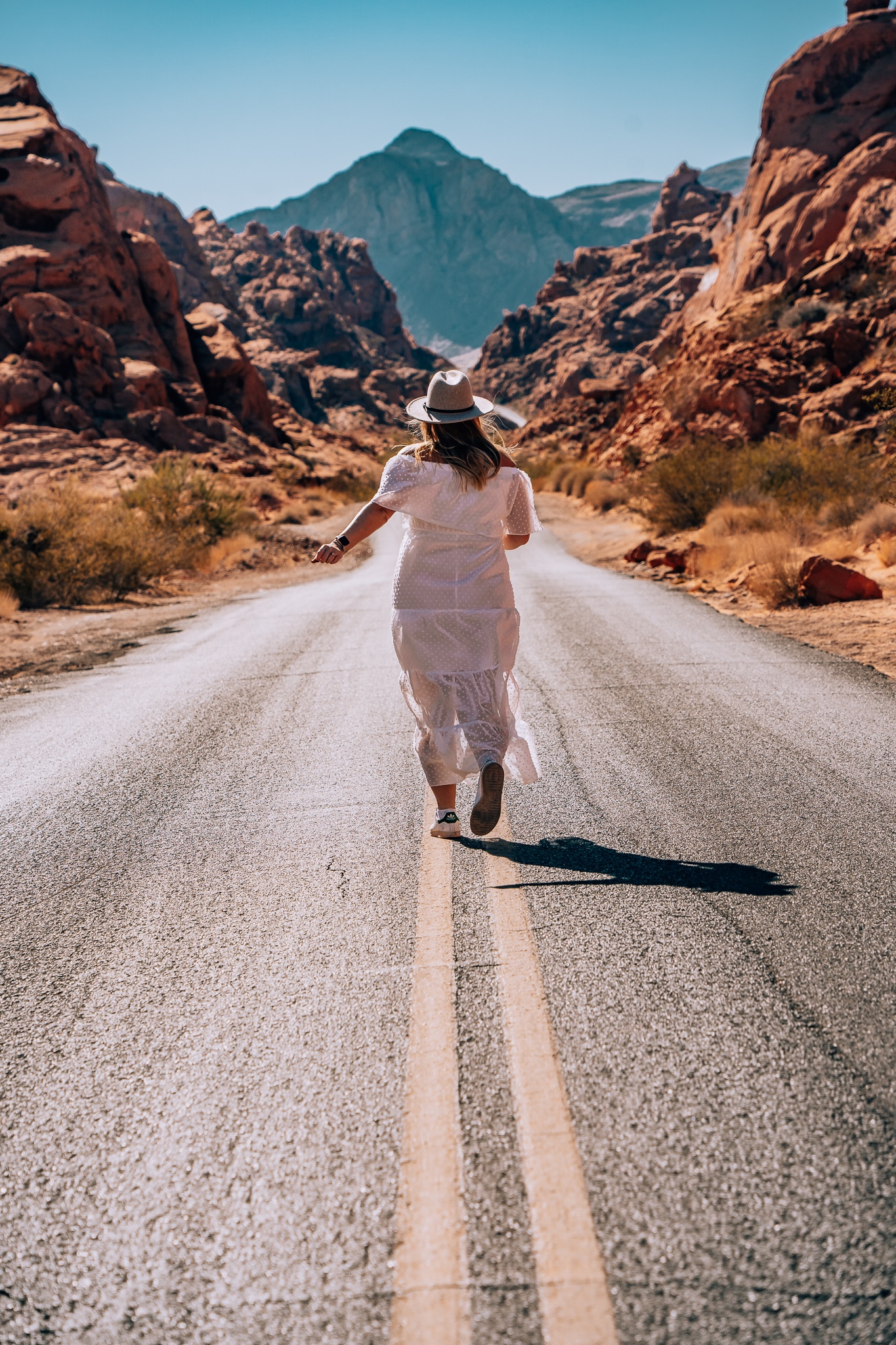 Woman running away in the middle of a road with red rocks all around