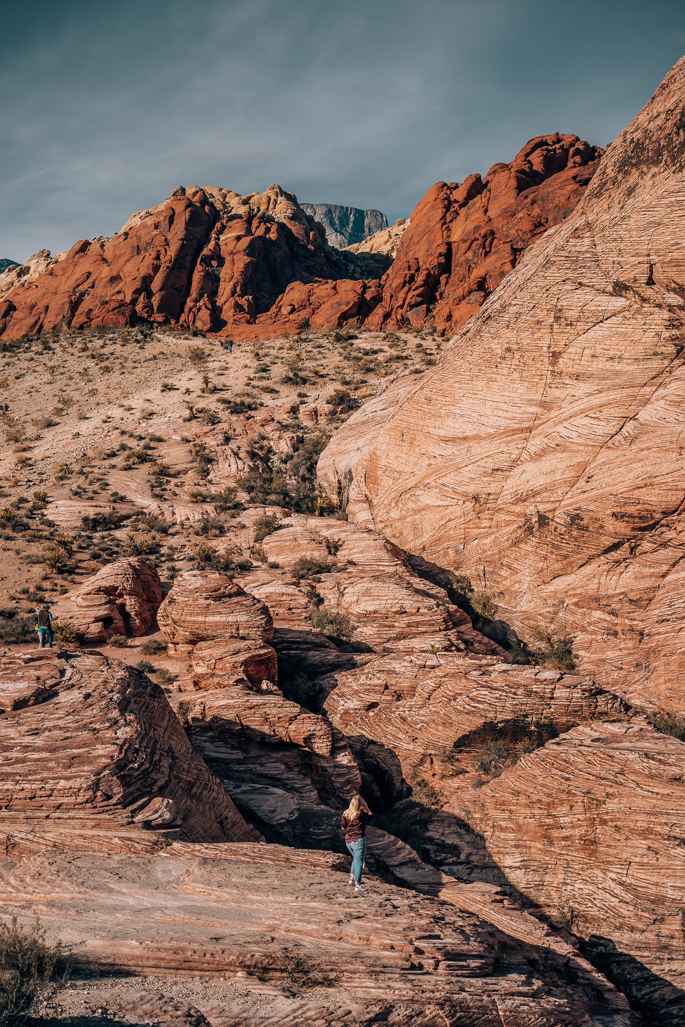 Woman standing at the base of some giant red rocks in Red Rock Canyon