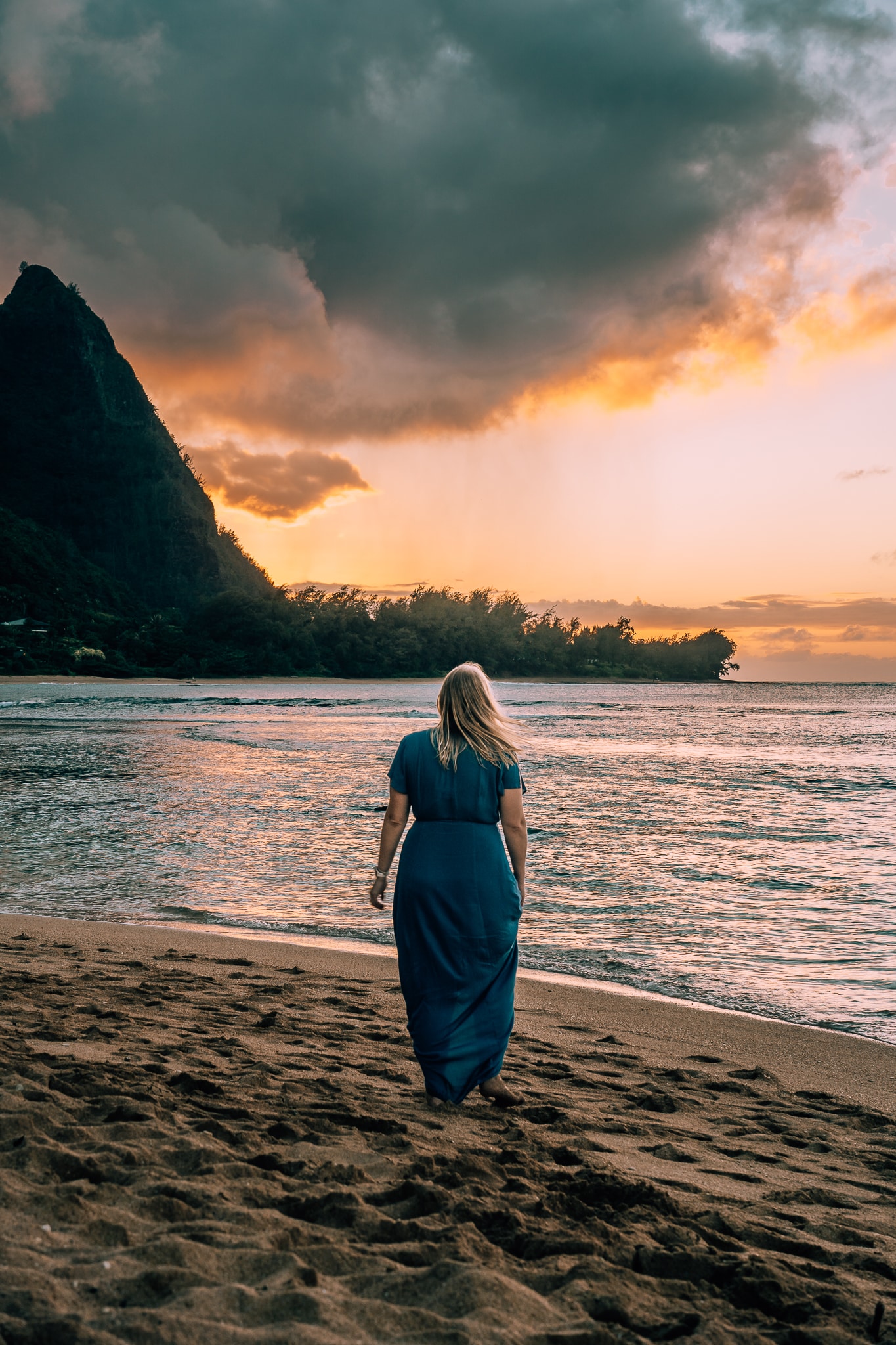 Woman standing on a beach looking to the mountain with the sun setting behind it