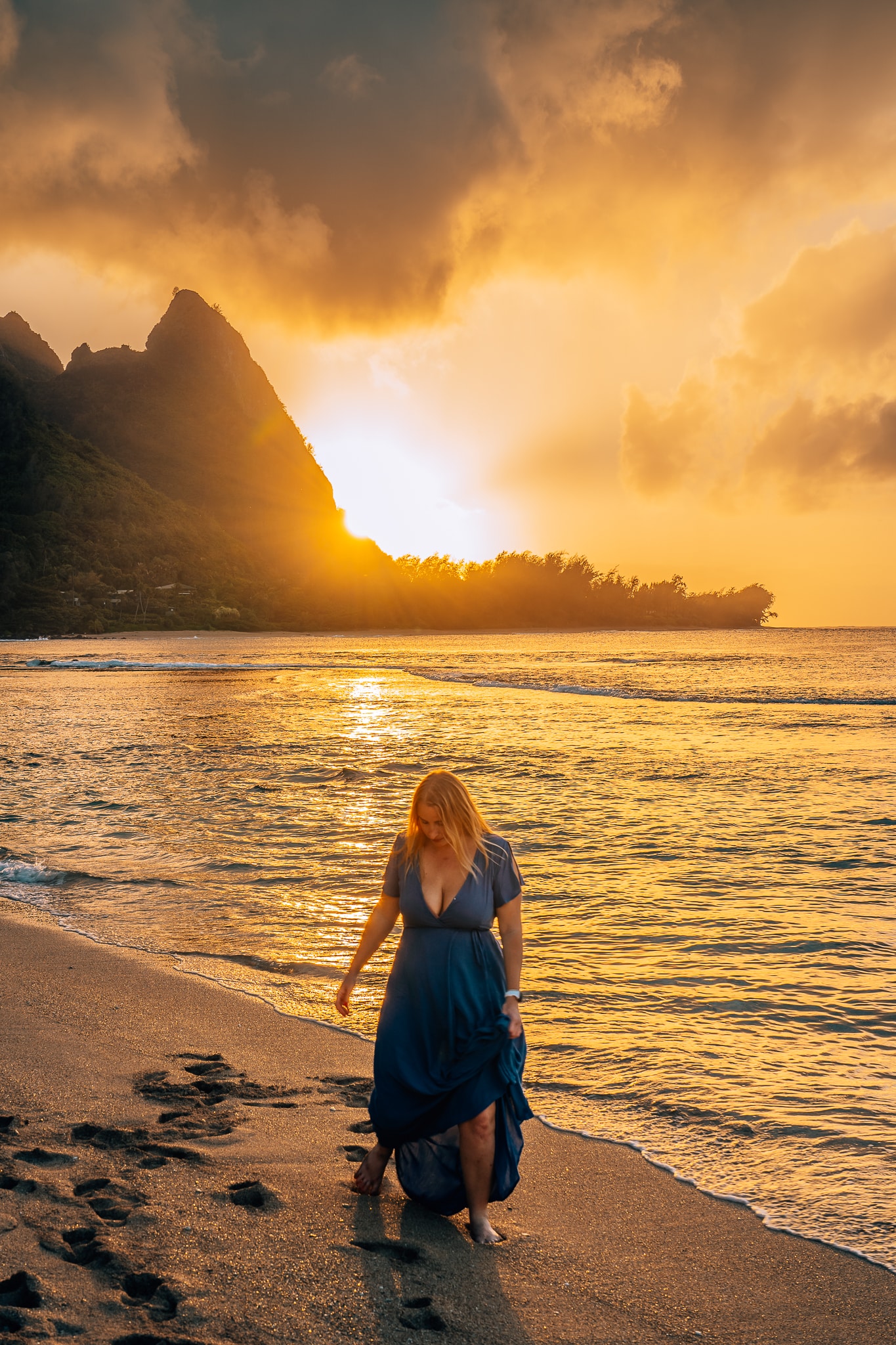 Woman standing on a beach in Kauai with the sun setting behind the mountain in the background