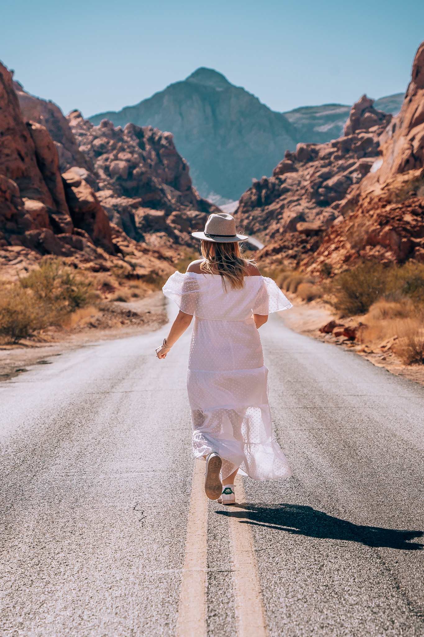 Woman running down the middle of the road with the red rock mountains in the background at Valley of Fire State Park