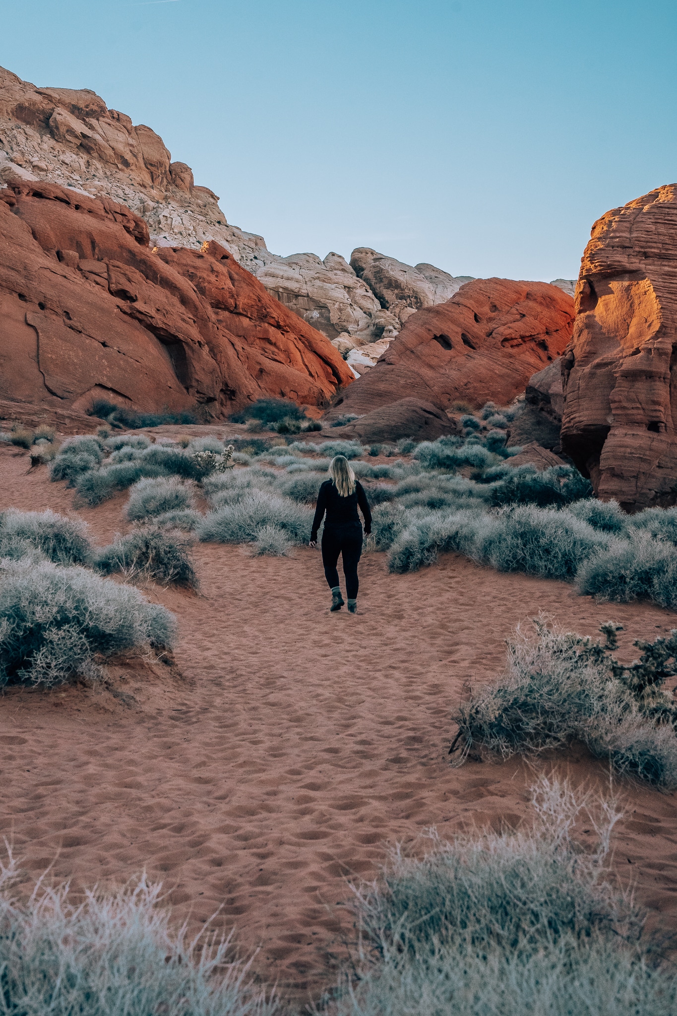 Woman walking in the sand through a hiking trail with red rocks in the background