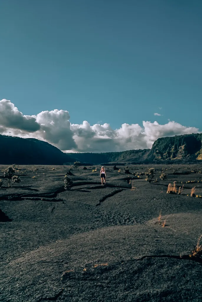 Woman in a white tank top and black shorts standing in the middle of a dried lava bed in the Kilauea Iki Trail in Volcanoes National Park on the Big Island of Hawaii