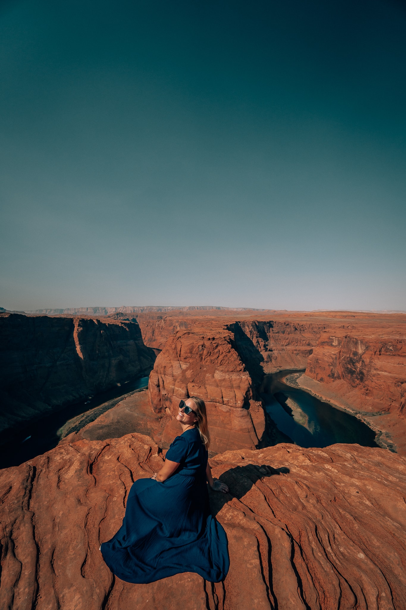 Woman in a blue dress sitting on the ground at Horseshoe Bend in Page, Arizona