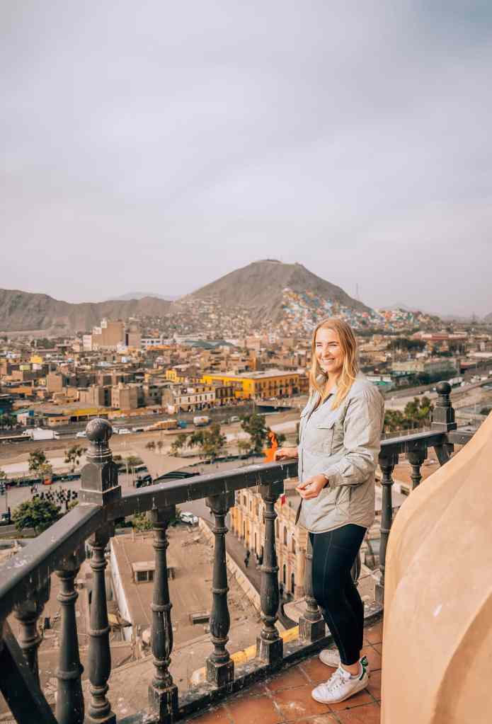 Woman standing atop the Convento Santo Domingo in Lima, Peru with the cityscape and a mountain in the background