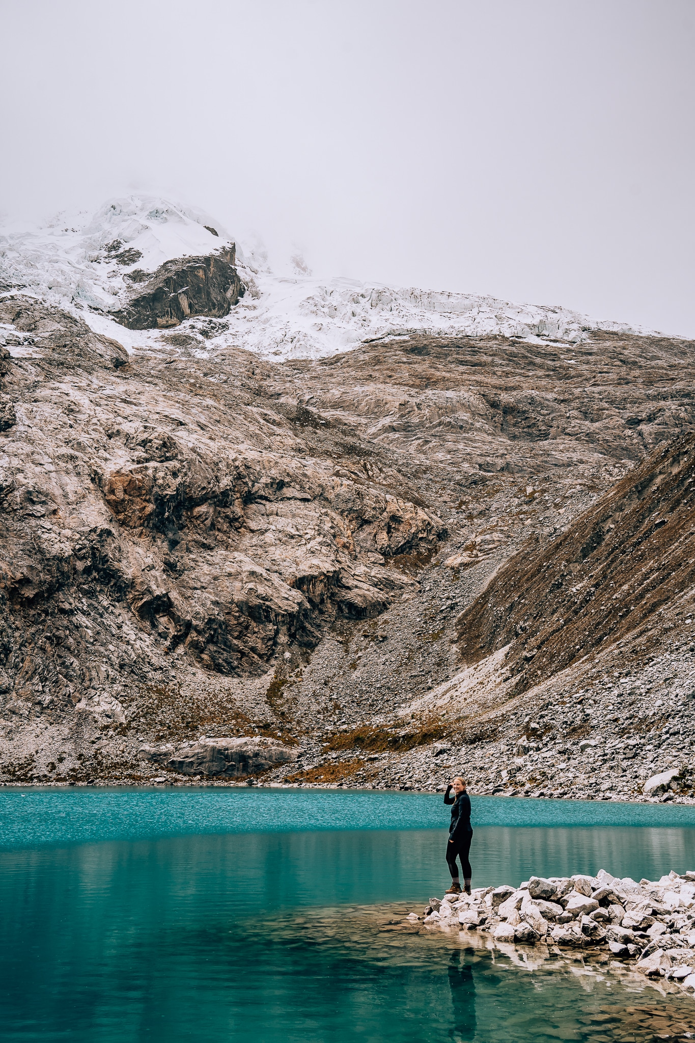 Woman standing on the shoreline of an incredibly blue lake with a snowcapped mountain in the back