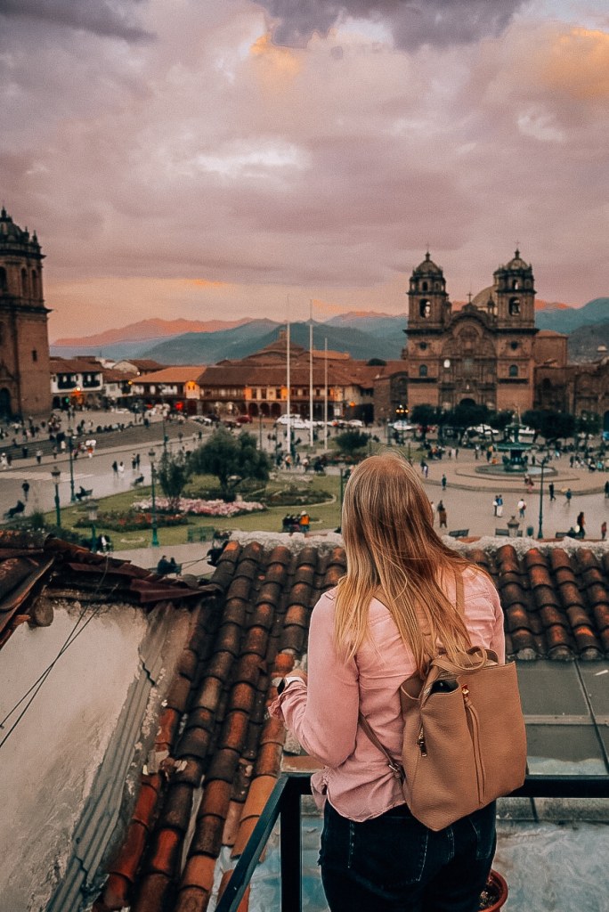 Woman standing on a terrace looking out toward the Plaza De Armas in Cusco during sunset