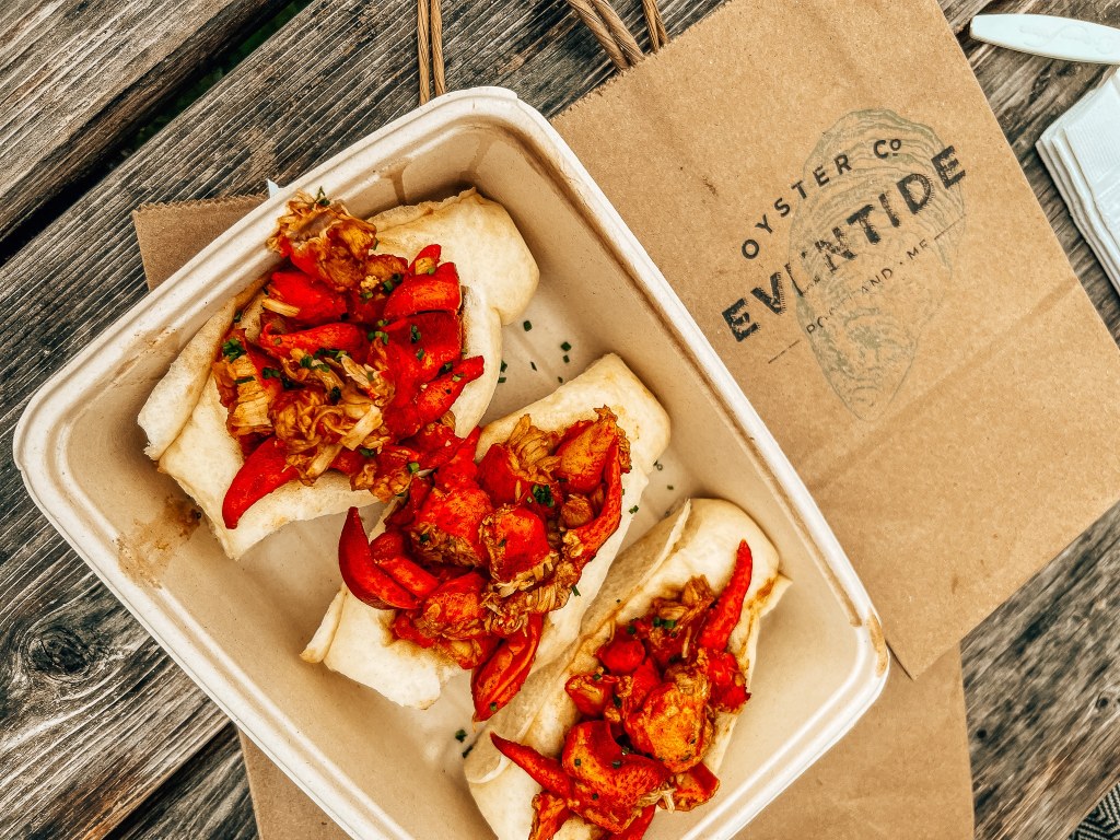 Lobster rolls in a to go container with a brown bag behind