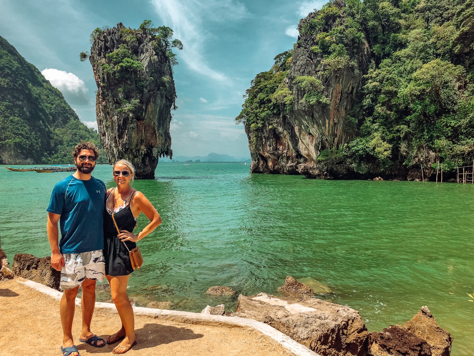 Smiling man and woman standing in front of James Bond Island, a very small but tall island, sticking out of the water in Thailand