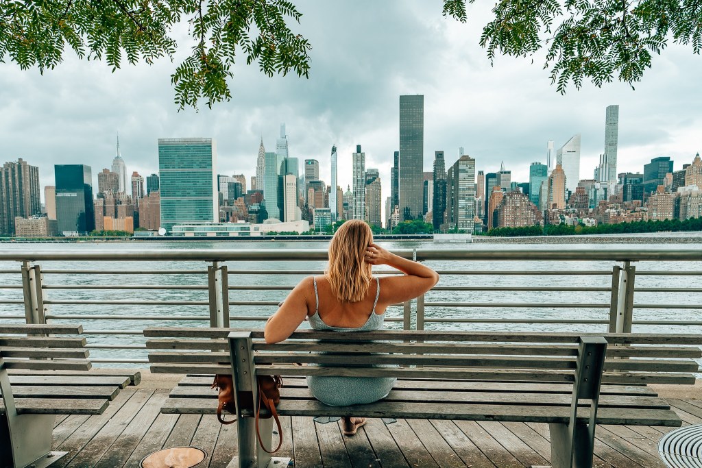 Woman sitting on a park bench looking out to the skyline of NYC