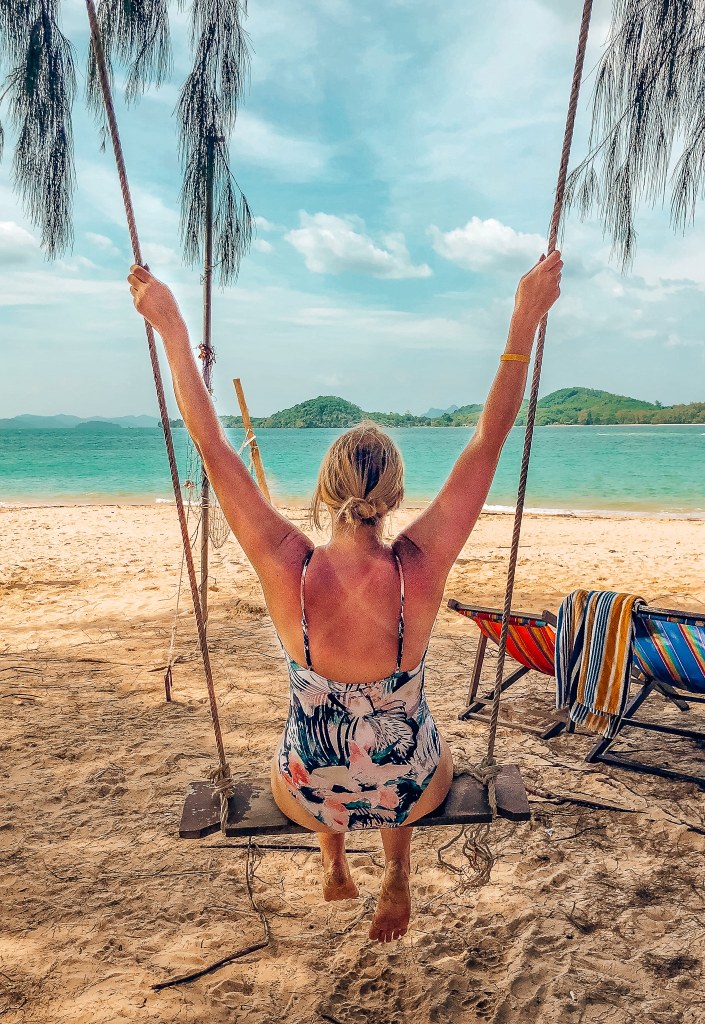 Woman in a swimsuit sitting in a swing looking out to the beach on Naka Noi island in Thailand