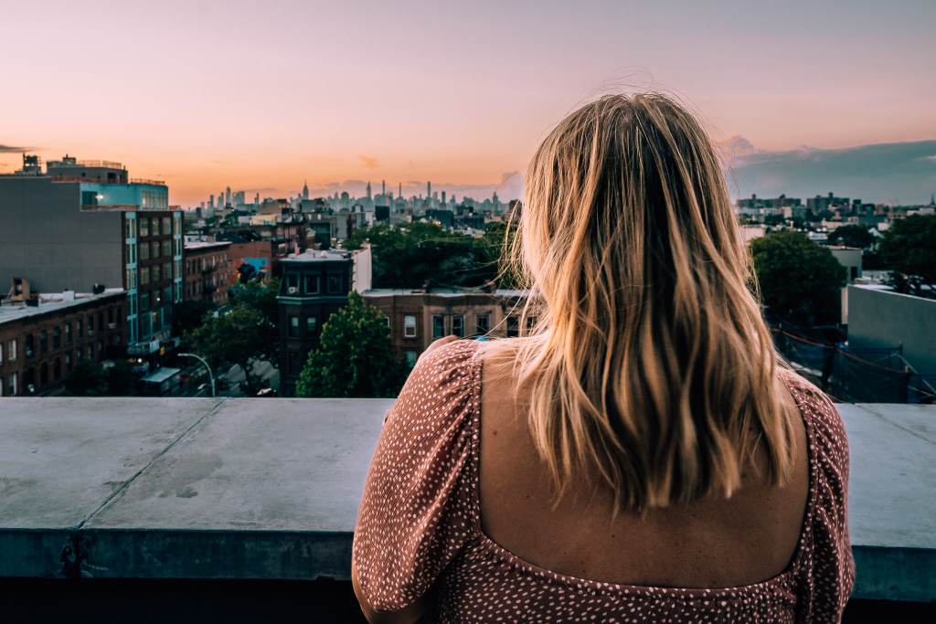 Woman standing on a balcony looking out to the New York City skyline at sunset