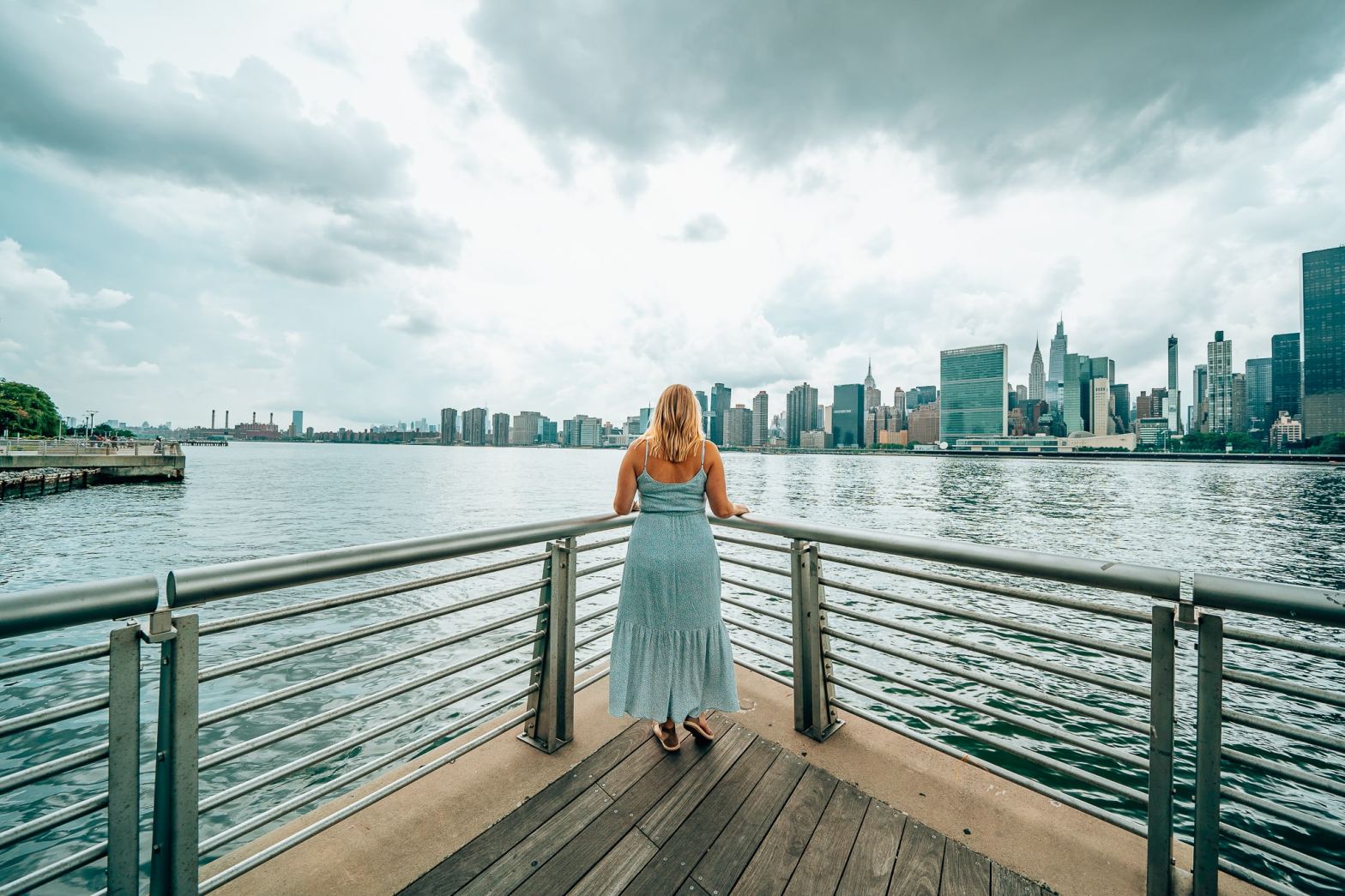 Woman standing in the corner of a deck in Hunter's Point South Park in Queens, New York, looking out to the NYC skyline