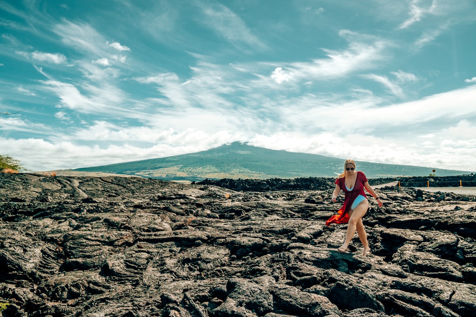Woman in a swimsuit and coverup walking over the lava bed that has flown down in front of Mauna Loa in the Big Island of Hawaii