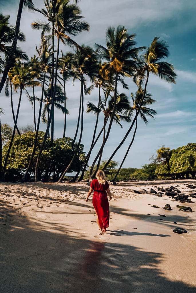 Woman walking on a beach in Hawaii walking away from the camera with palm trees in the background