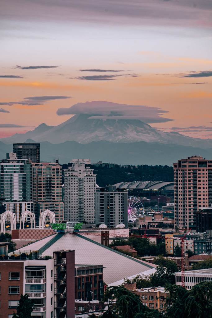 In the distance is Mount Rainier with a cloud hanging over the top, with Seattle's city in front of it and a sunset sky behind