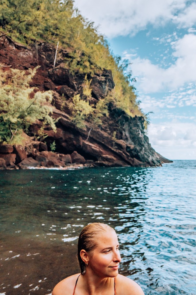 Woman sitting in the water of Maui's red sand beach with the cliff in the background