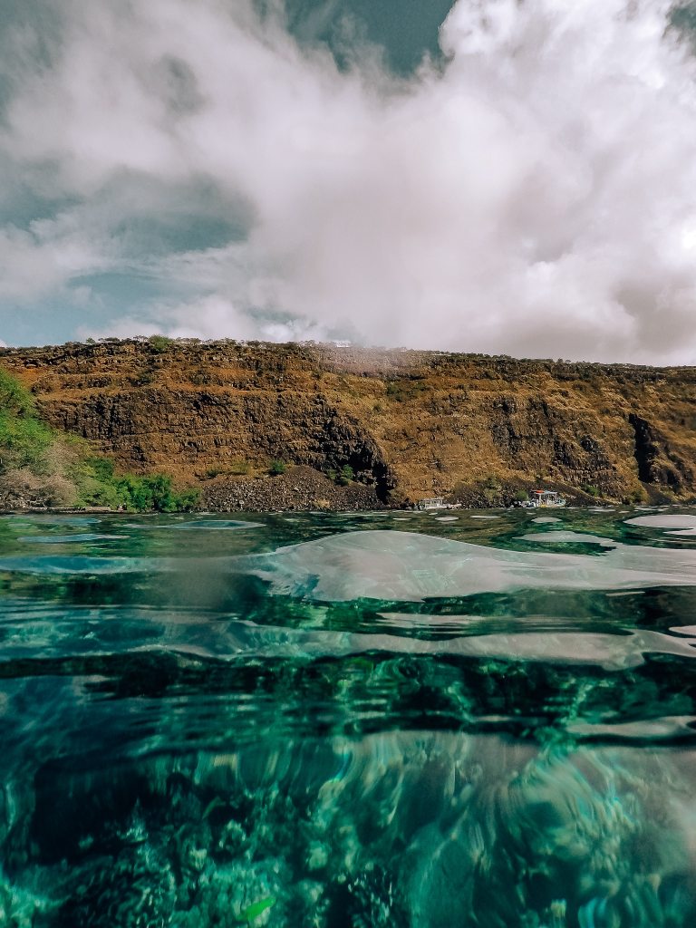 Photo taken from in the water so the water is in the foreground and the Big Island cliffs are in the background