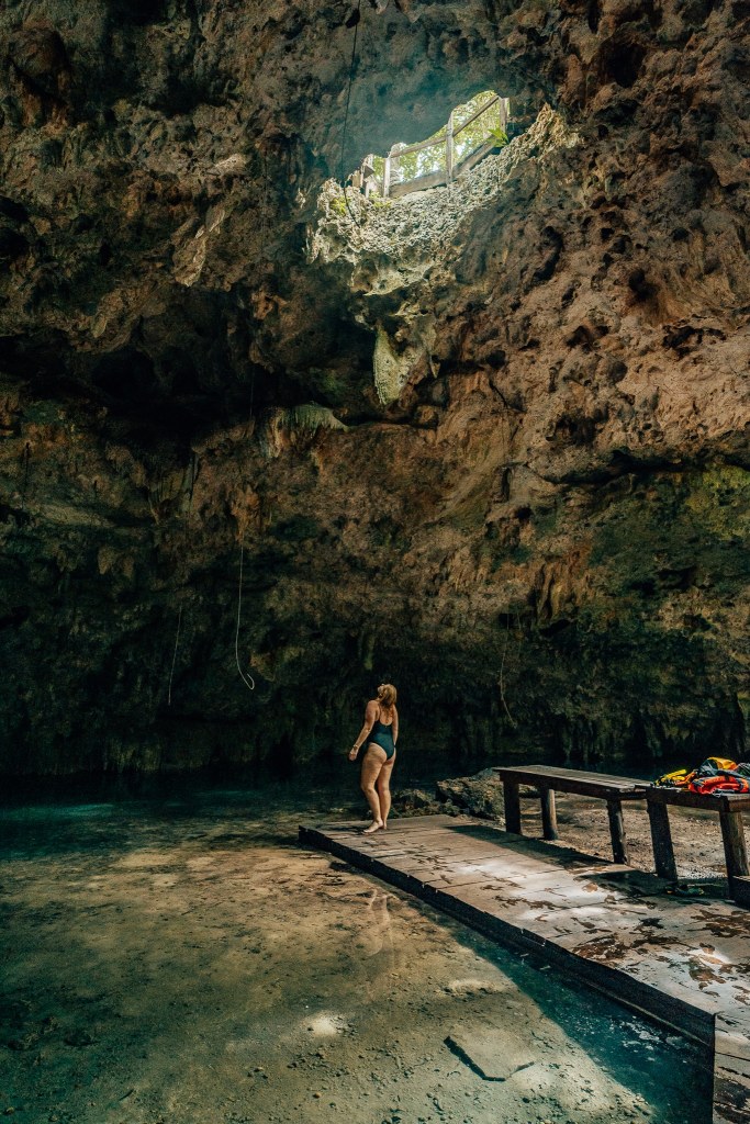 Woman standing under a hole in the ceiling of a cavernous cenote near Tulum, Mexico