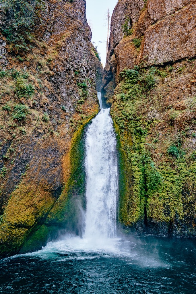 Moss-covered rock wall with a double-layer waterfall falling in between it into a pool