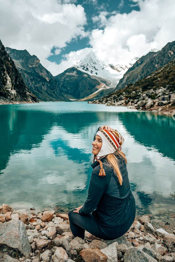 Woman sitting along the lakeshore of Laguna Paron with the mountain in the background